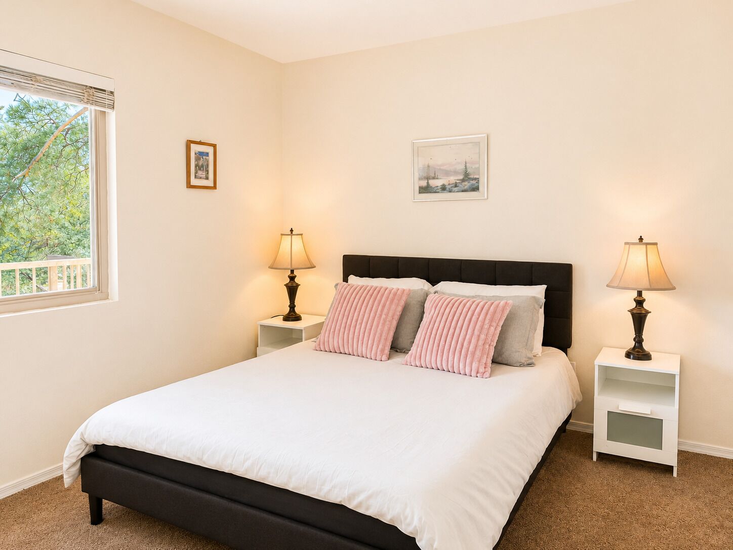 A bedroom with a bed, two bedside tables, two lamps, and two framed pictures on the wall.