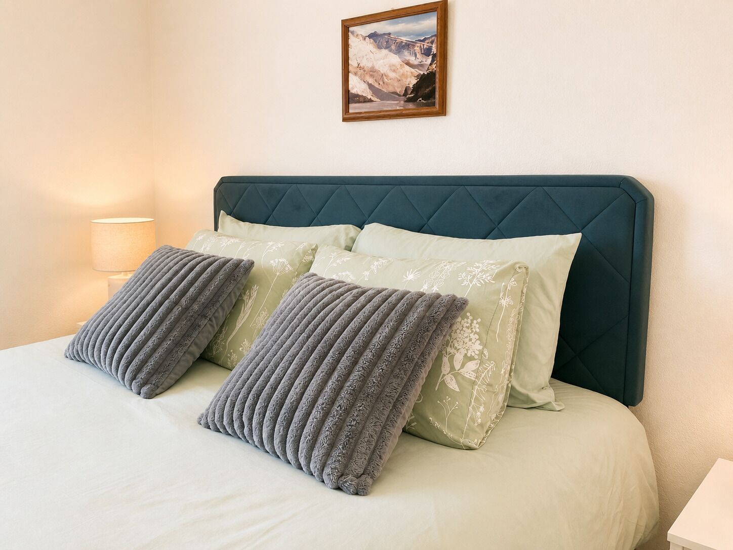 Un lit avec une tête de lit matelassée, deux oreillers et une lampe de chevet.