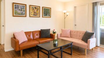 Un salon avec un canapé en cuir marron, un canapé rose pâle, une table basse noire et trois œuvres d’art encadrées accrochées au mur.