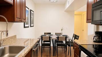 A compact kitchen with a dining area, stainless steel sink, wooden cabinets, and a black microwave.