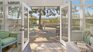 Puerta abierta que da a una terraza con mobiliario exterior, vistas a árboles y cielo despejado.