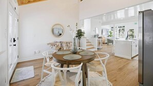 Una cocina moderna con armarios blancos, techo de madera y comedor con una mesa redonda y sillas blancas.