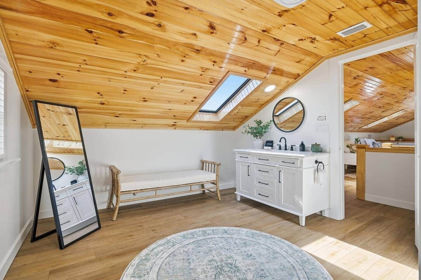 Un dormitorio tipo loft con techo de madera, tragaluz, cama, tocador y alfombra redonda.