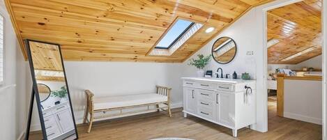Un dormitorio tipo loft con techo de madera, tragaluz, cama, tocador y alfombra redonda.