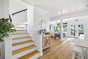 A modern interior with a wooden staircase, a kitchen area, and a dining space with a view.