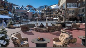 A snow-covered outdoor seating area with fire pits, surrounded by buildings with snow-covered roofs. - Spacious 3-bedroom condo in superb Beaver Creek. (Beaver Creek)