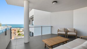 En balkong med ett träbord och två stolar, med utsikt över stadsbilden och havet.