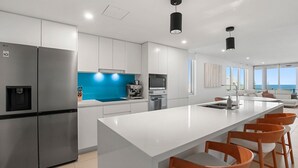Ett modernt kök med en stor köksö, rostfria vitvaror och ett blått stänkskydd.