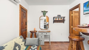 A compact living space with a bed, a desk with a mirror, a small stool, and a dining area with stools.