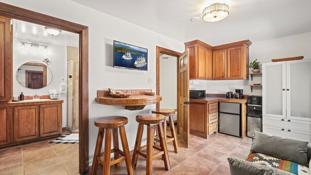 A modern kitchen with wooden cabinets, a built-in microwave, and a coffee maker. There is a round mirror above the sink and a wooden bar stool area.