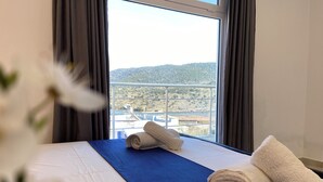 Habitación de hotel con cama, vista a un paisaje montañoso y ventana con cortinas.