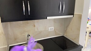 Una cocina moderna con armarios negros, un lavamanos de acero inoxidable y un protector contra salpicaduras de mármol.