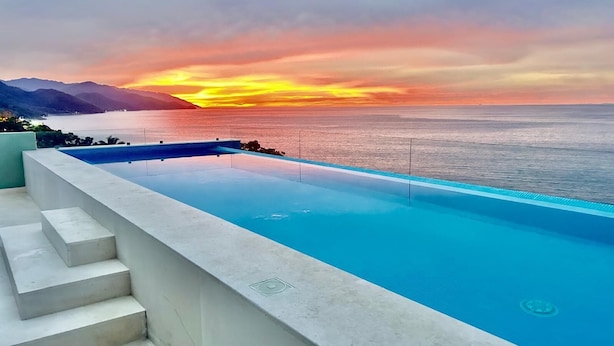 Ein Infinity-Pool mit freiem Blick auf das Meer und die Berge im Sonnenuntergang.