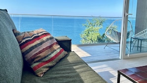 Ein Balkon mit Meerblick, eine Couch mit gestreiftem Kissen und ein Sessel.