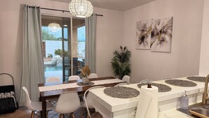 Un coin repas avec une table dressée pour quatre personnes, des chaises blanches, une nappe blanche et un centre de table décoratif.