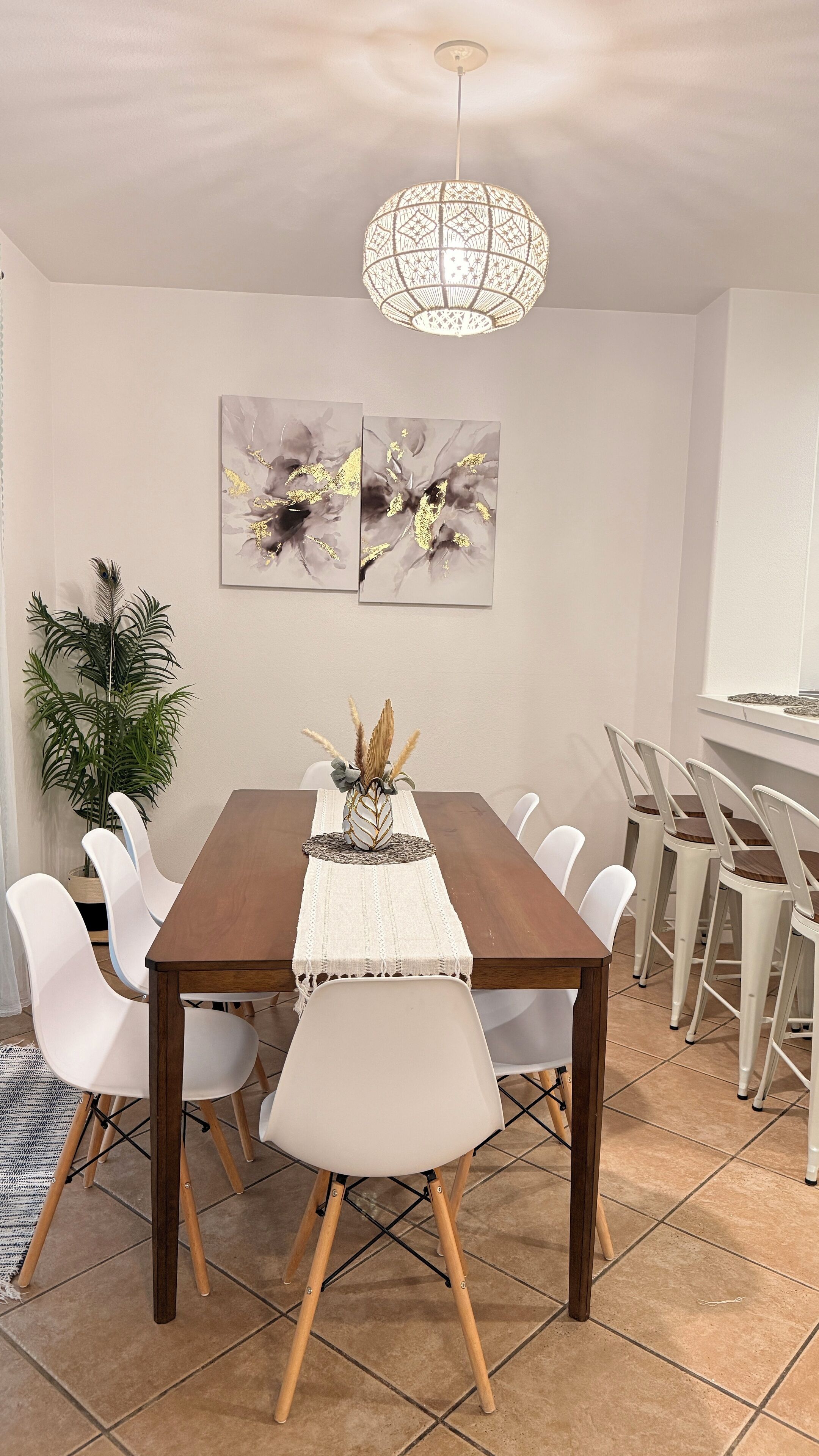 A dining area with a wooden table, white chairs, a white pendant light, and two abstract paintings on the wall.