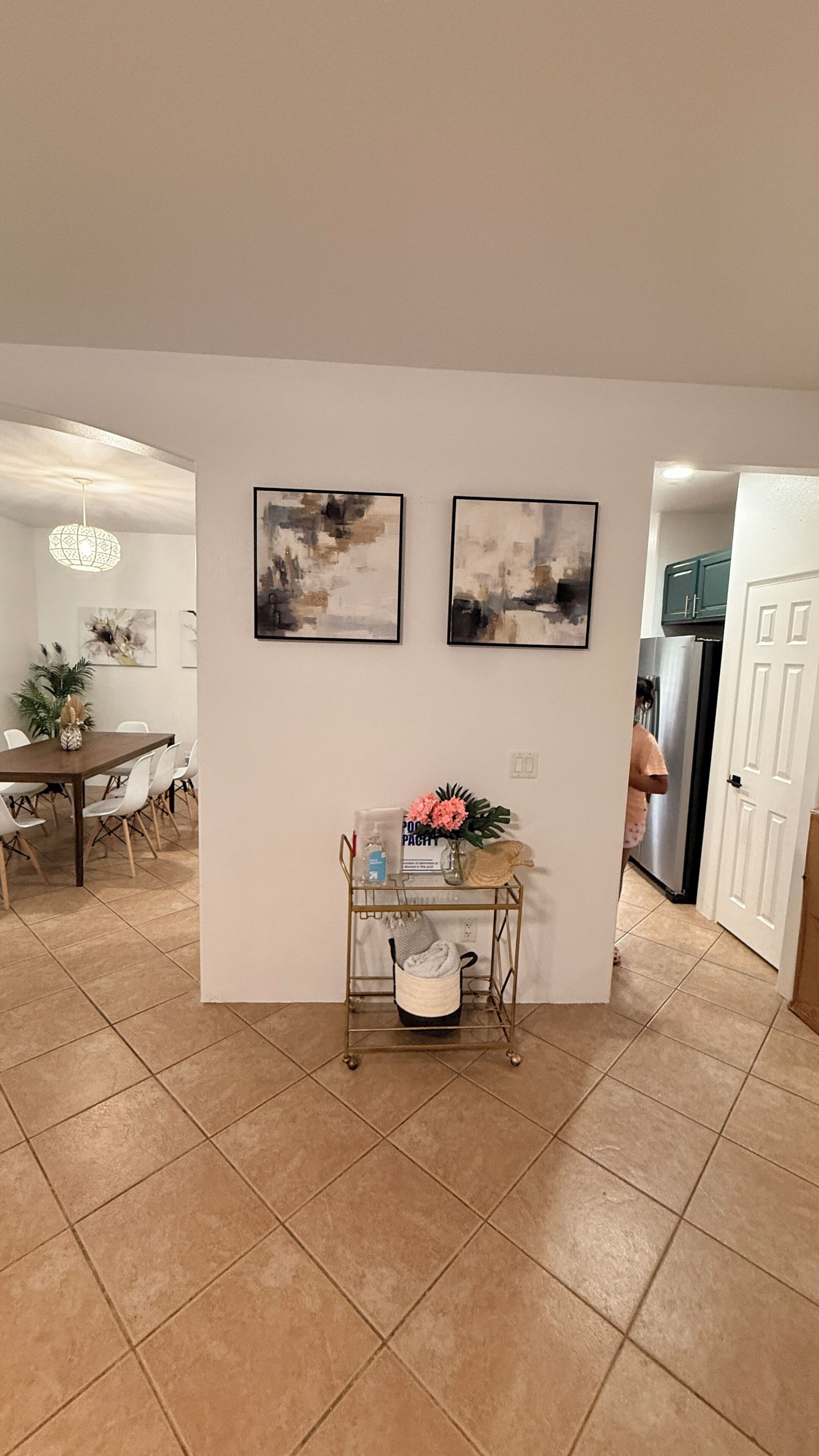 Un coin repas avec une table et des chaises, une petite table d’appoint avec un vase et une bouteille, et deux tableaux abstraits accrochés au mur.