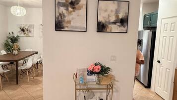 Un coin repas avec une table et des chaises, une petite table d’appoint avec un vase et une bouteille, et deux tableaux abstraits accrochés au mur.