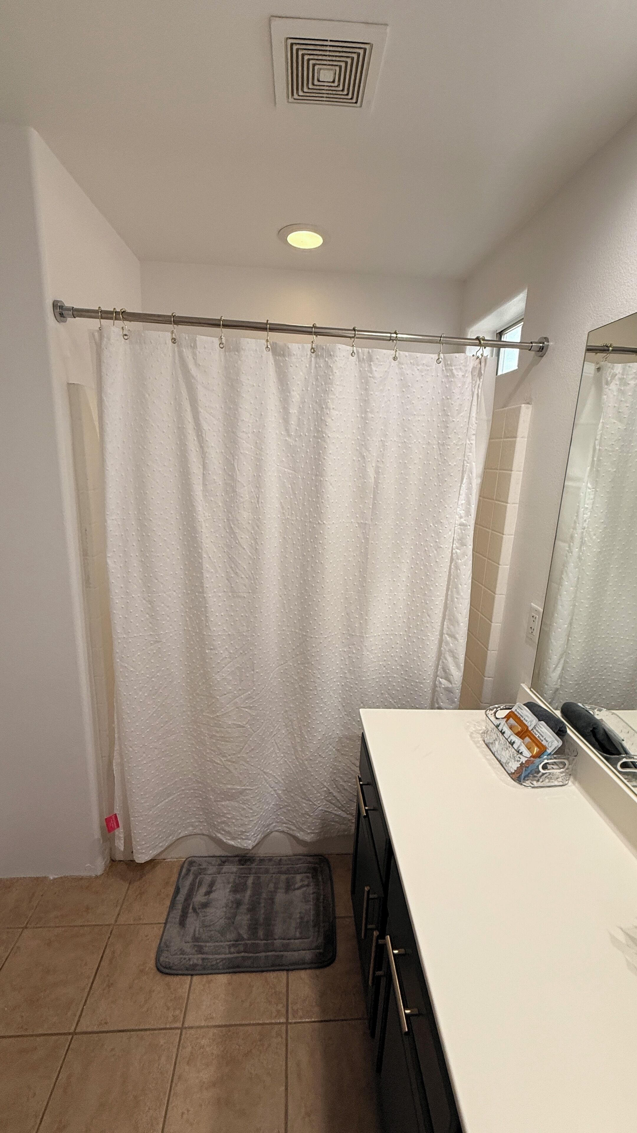 A bathroom with a shower curtain, a towel rack, a mirror, and a sink with toiletries.