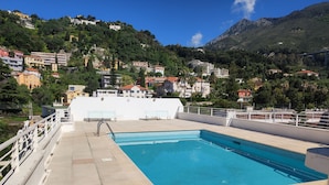 En swimmingpool med udsigt over en by på en skråning og bjerge i baggrunden.