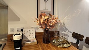 Un tavolo da pranzo con una macchina per caffè Nespresso, un'opera d'arte raffigurante un bicchiere da cocktail, un vaso con fiori secchi e un vassoio con bicchieri da vino.