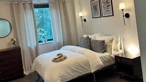 Una camera da letto con un letto, una cassettiera, un comodino, una lampada e una finestra con tende.