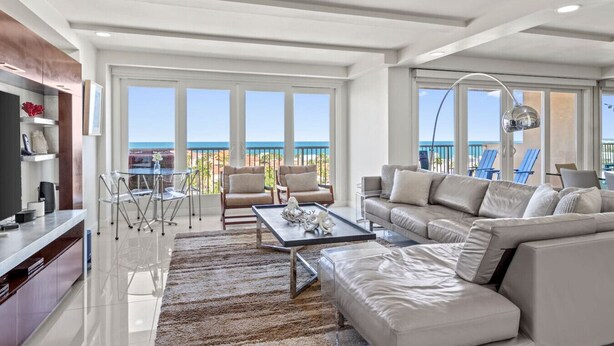 A spacious living room with a large sofa, a coffee table, and a dining area with chairs. There are large windows offering a view of the ocean. - Where the Sky Meets the Sea – Luxury Dream Views (South Padre Island)
