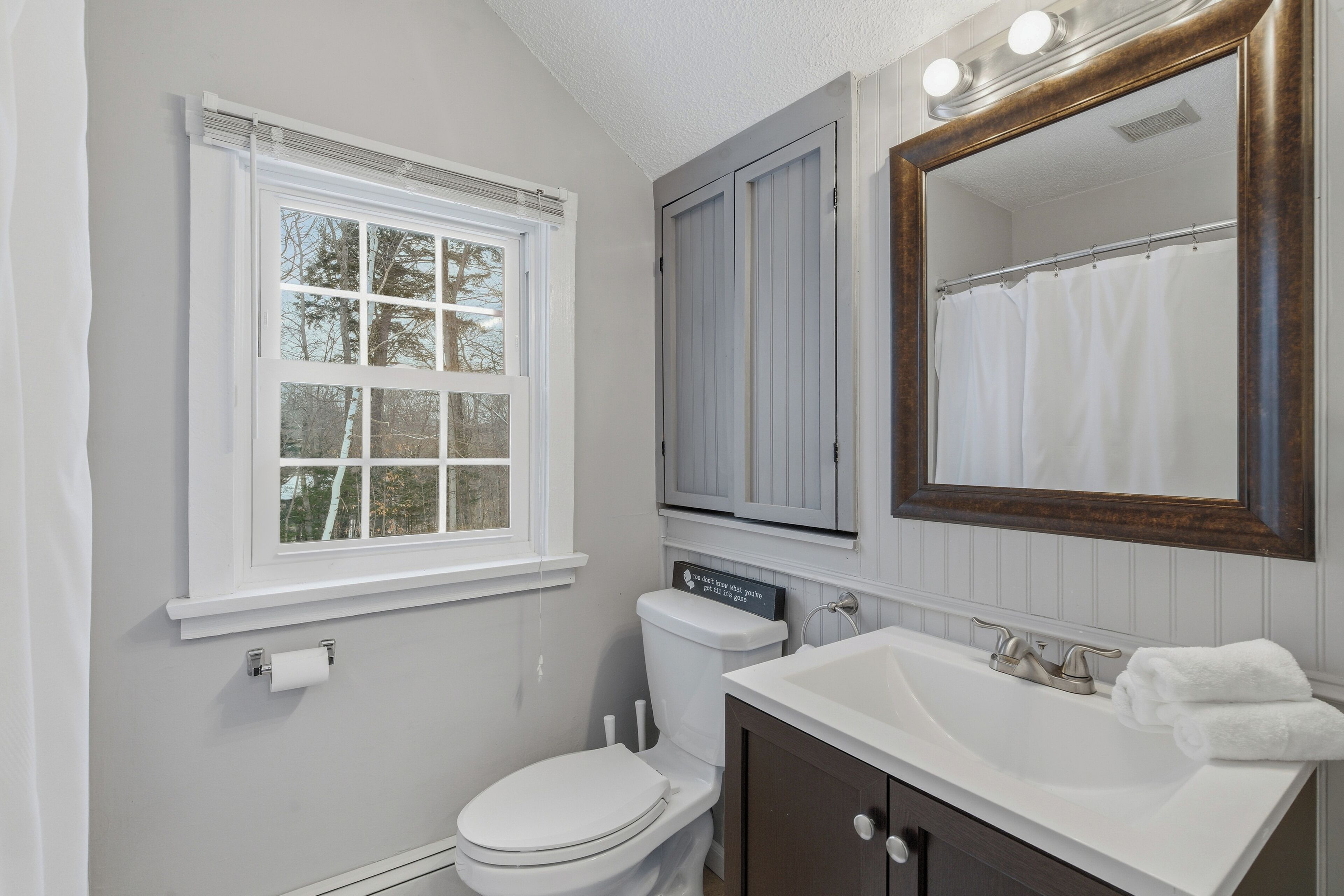 Ein Badezimmer mit einer weißen Toilette, einem Waschbecken mit Spiegel darüber und einem Fenster mit Jalousien.