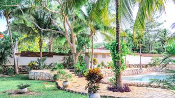 Un jardín con piscina, palmeras y un muro de piedra.