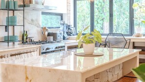 A modern kitchen with a marble island, wooden bar stools, and hanging pendant lights. - Private Home with Luxury Pool and Outdoor Living (Yalcón)