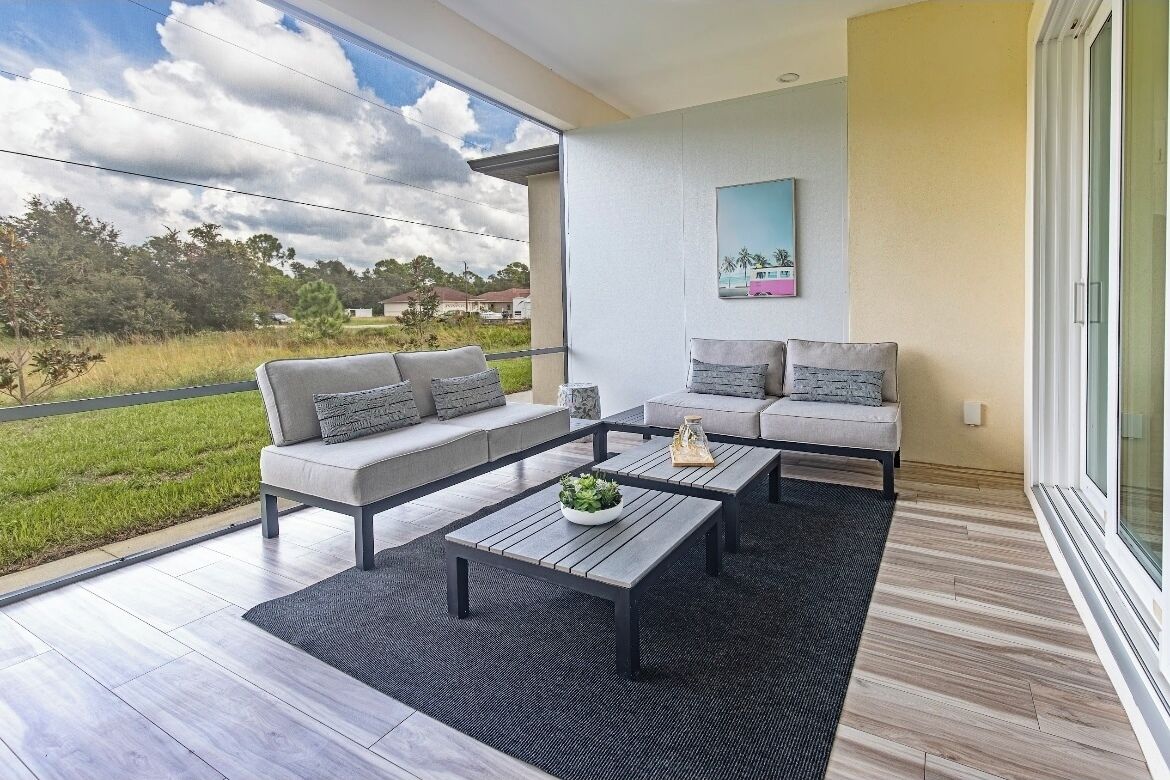 A modern balcony with a grey sofa, a wooden coffee table, and a view of a green landscape.