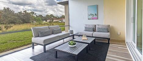 A modern balcony with a grey sofa, a wooden coffee table, and a view of a green landscape.
