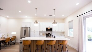 A modern kitchen with white cabinets, stainless steel appliances, and a central island with bar stools. - Luxury Retreat in Reunion w/Private Pool and Hot Tub - Sleeps 10 (Kissimmee)