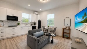 A modern kitchen with white cabinets, a black microwave, and a dining area with a gray sofa and chairs. - Private Cozy and relaxing 1-bedroom unit with living room kitchen full bath more (North Port)