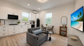 A modern kitchen with white cabinets, a black microwave, and a dining area with a gray sofa and chairs. - Private Cozy and relaxing 1-bedroom unit with living room kitchen full bath more (North Port)