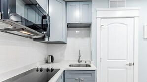 A modern kitchen with a black stovetop, white tiles, and light blue cabinets. - S. Philly Studio Minutes - Center City Passyunk Sq and More! (Philadelphia)