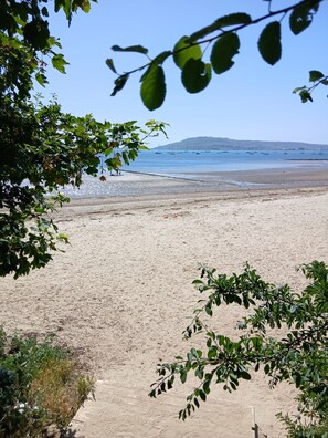 Ein Strand mit blauem Himmel, sandigem Ufer und Booten in der Ferne.