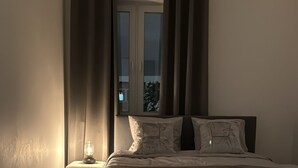 Un dormitorio con cama, cortinas, mesita de noche y ventana.