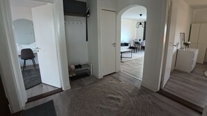 Amplia sala de estar con un gran tapete, una mesa de comedor con sillas y una zona de cocina con refrigerador y alacenas.