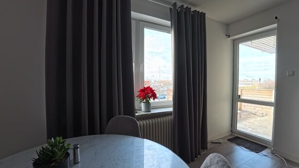 Una habitación moderna con una mesa de mármol, una planta en maceta, un radiador y una ventana con cortinas.