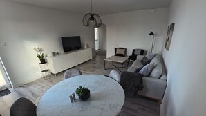 Una sala moderna con una mesa de comedor de mármol, sofá gris y televisor sobre un mueble blanco.