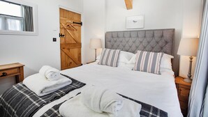 A neatly made bed with a grey headboard, striped pillows, and rolled towels.