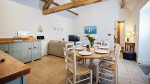 A cozy kitchen with a dining area, wooden beams, a TV, and a painting on the wall.