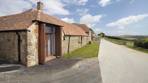 A row of stone cottages with brick roofs, a paved driveway, and a rural landscape in the background.