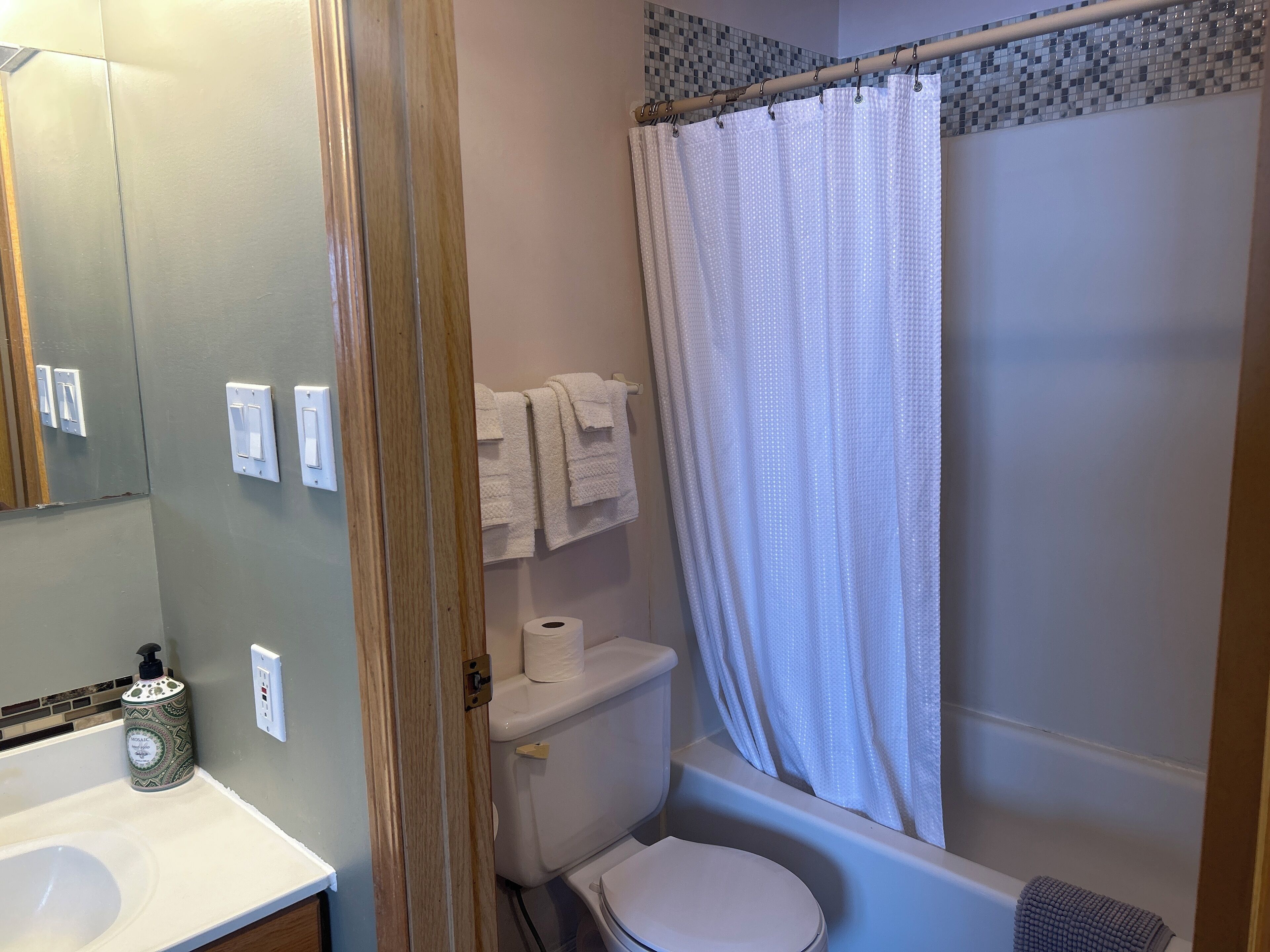 Een badkamer met toilet, bad, douchegordijn, wastafel en spiegel.