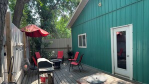 Une terrasse en bois avec des meubles d’extérieur, un barbecue et un parasol rouge.