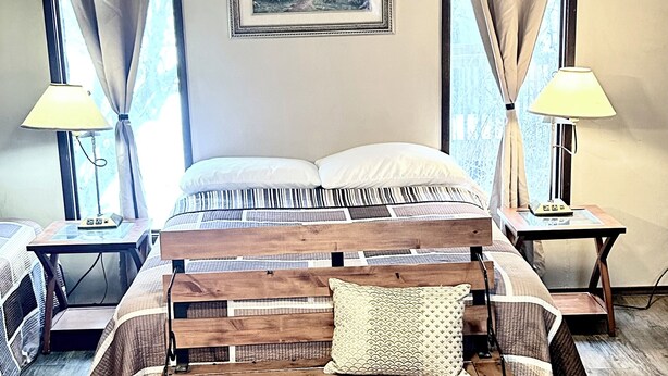 Une chambre à coucher avec un lit en bois, deux tables de chevet avec des lampes, un tableau encadré au mur et une fenêtre avec des rideaux.