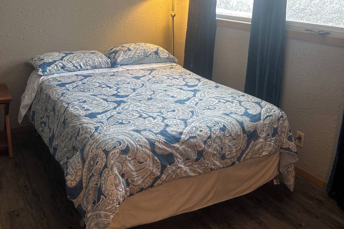 A bedroom with a bed, a nightstand, a lamp, and a window with curtains.