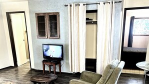 Un salon avec un téléviseur, deux canapés, une petite table et une fenêtre avec des rideaux.