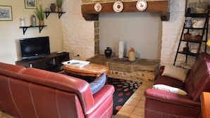 A living room with a stone fireplace, leather sofas, a television, and decorative shelves. - Camélia de kerguével (Plonévez-Porzay)